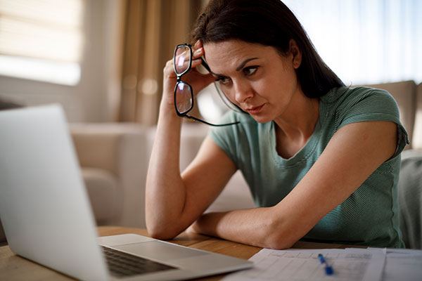 Frau mit Brille in der Hand die in einen Laptop schaut